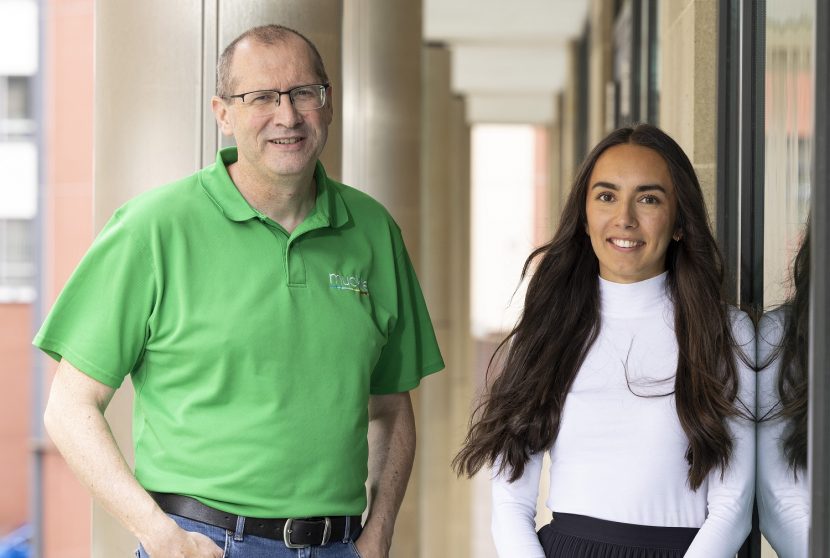 Two members of Muckle LLP team stood facing camera (medium close-up) one older man with green polo top and glasses, on the right is a Imaan wearing a white turtle neck top.