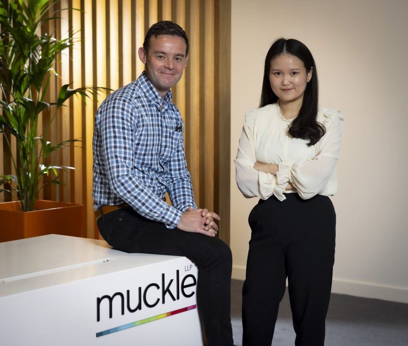 Adam Aston sat on Muckle LLP branded desk and Zi Chuen Gwi stood next to him with arms folded.