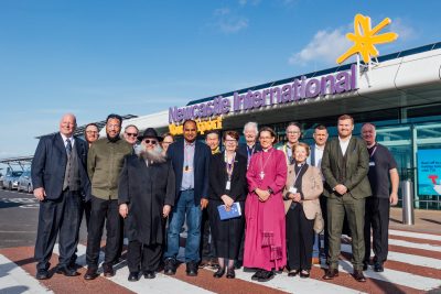 Senior management from Newcastle International Airport, the Airport Chaplains and faith leaders in large group in front of the entrance to Newcastle Airport