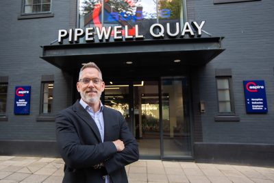 Tom standing outside of Aspire’s Quayside based HQ. He is smartly dressed, looking at the camera with his arms crossed.