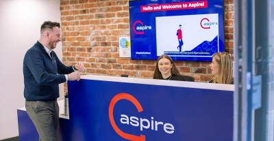 Man stood in front of Aspire reception desk laughing with two people who are sat behind desk.