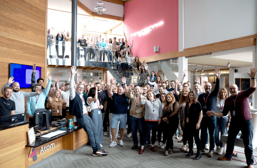 Large group of people in a spacious Atom Bank office reception all cheering towards the camera.