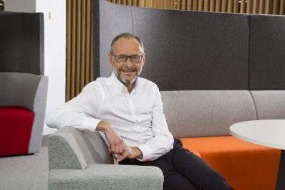 Hugh sat casually on a sofa smiling to camera.