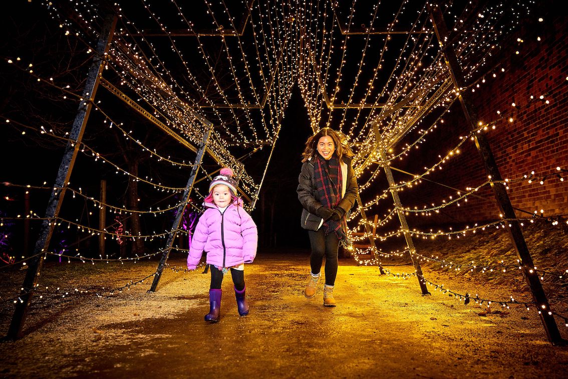 Adult and child running through a tunnel of string fairy lights.