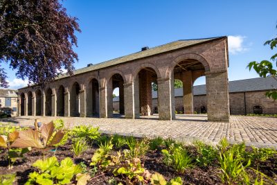 Dutch Barn building with rounded archways surrounded by gardens.