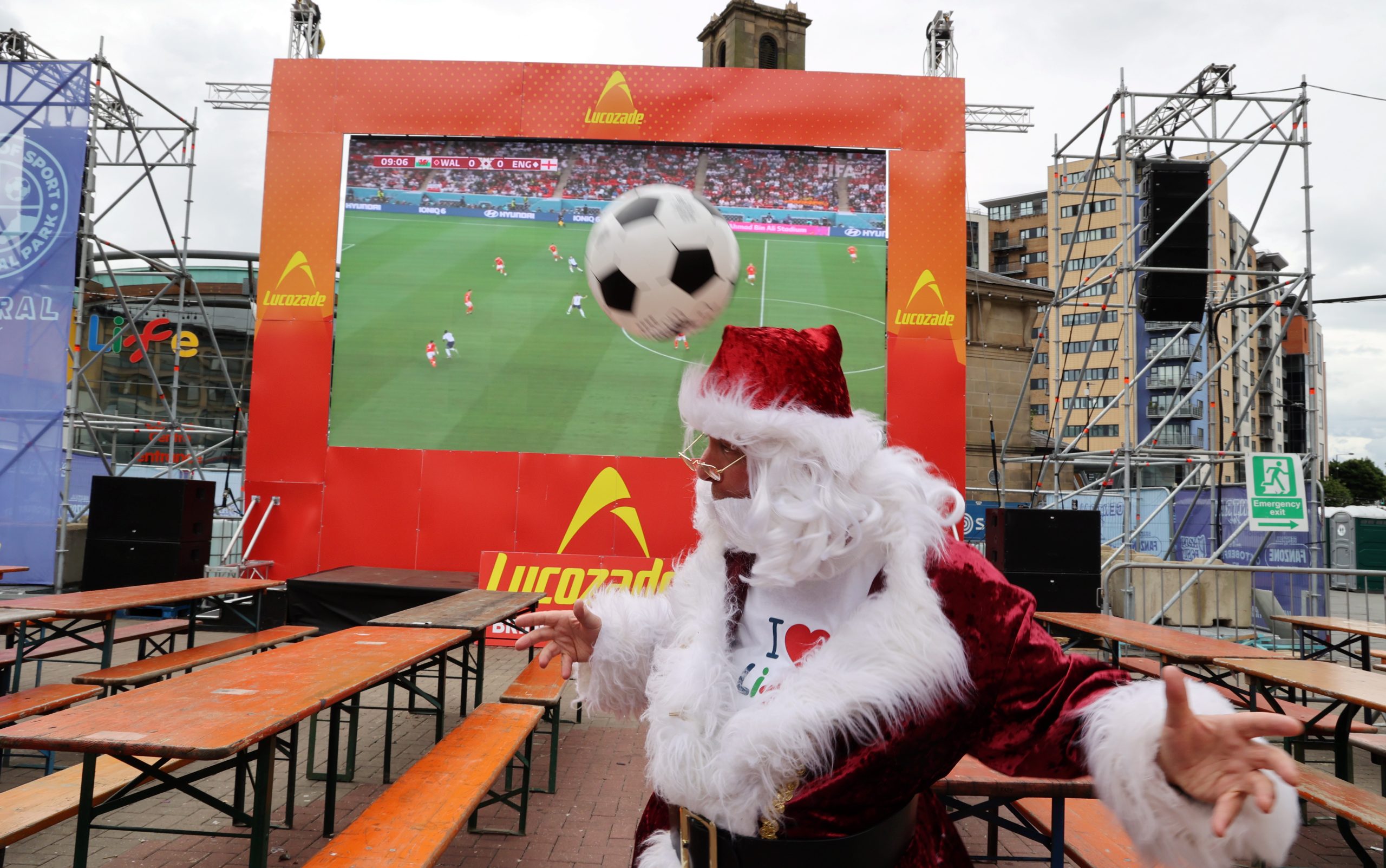 Person dressed as Santa headering a football in front of a big-screen