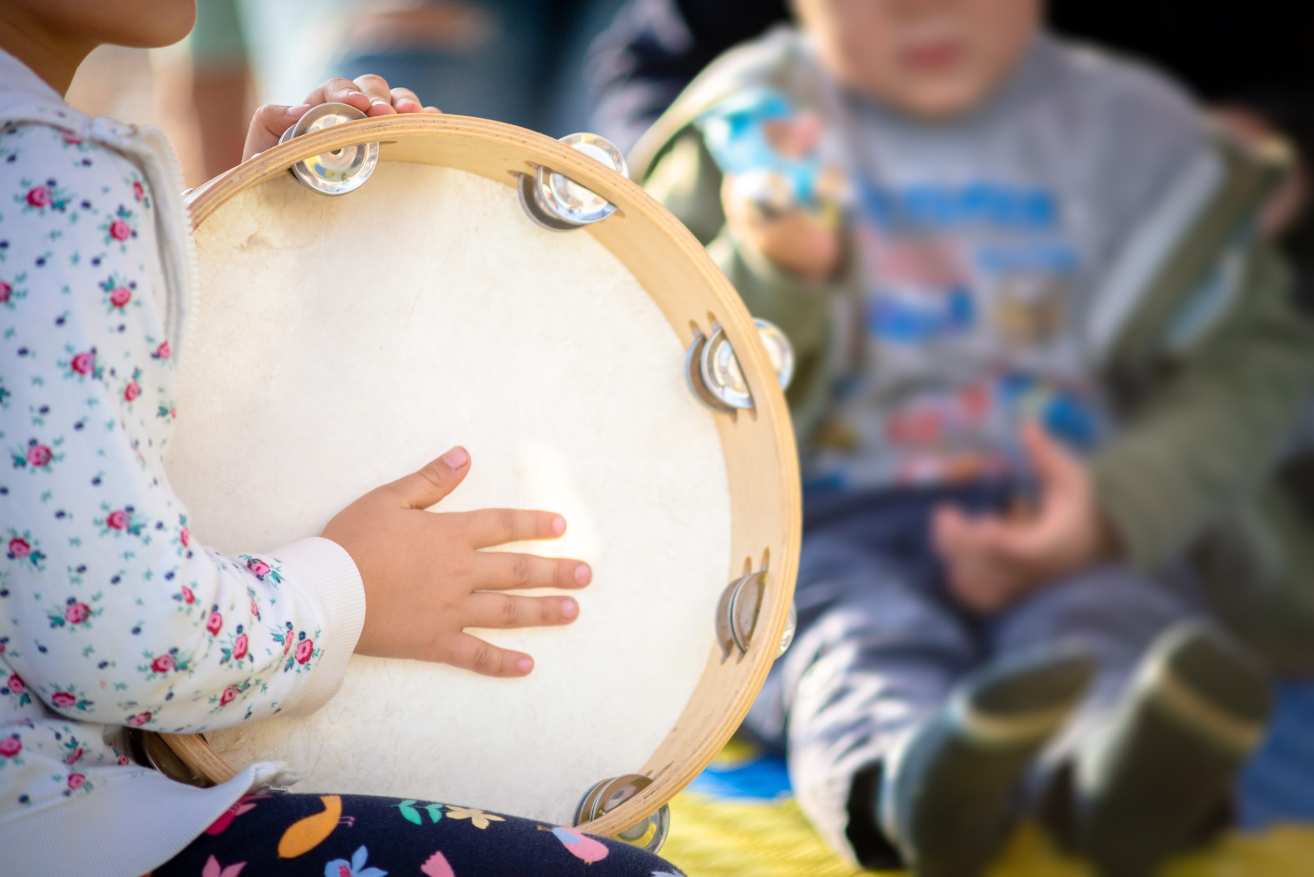 Image of two young children sat one is playing with a tamborine.