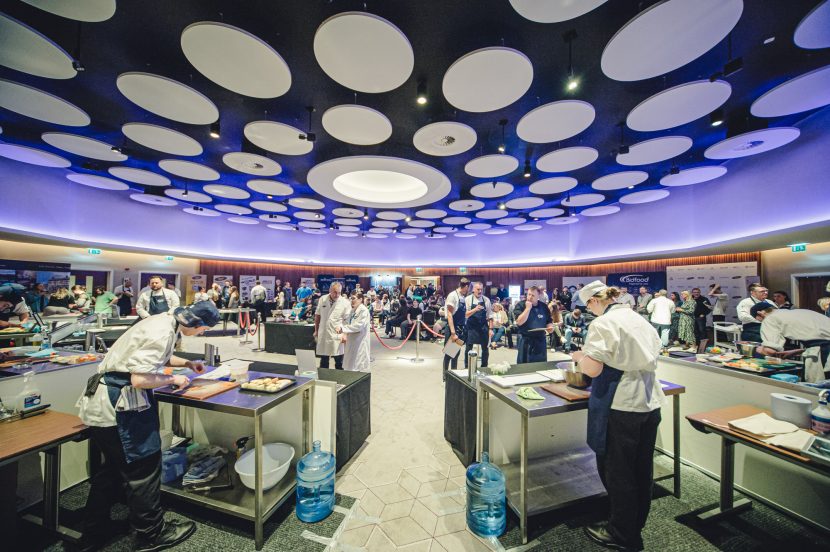 Chef competition taking place in front of audience and judges looking at the chefs in action.