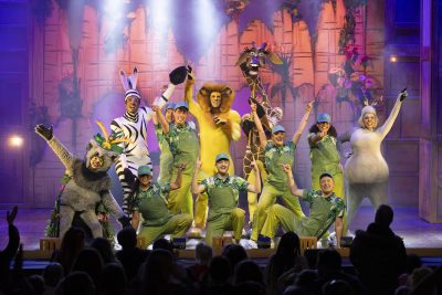 Cast of Madagascar The Musical performing on stage together in full costume.