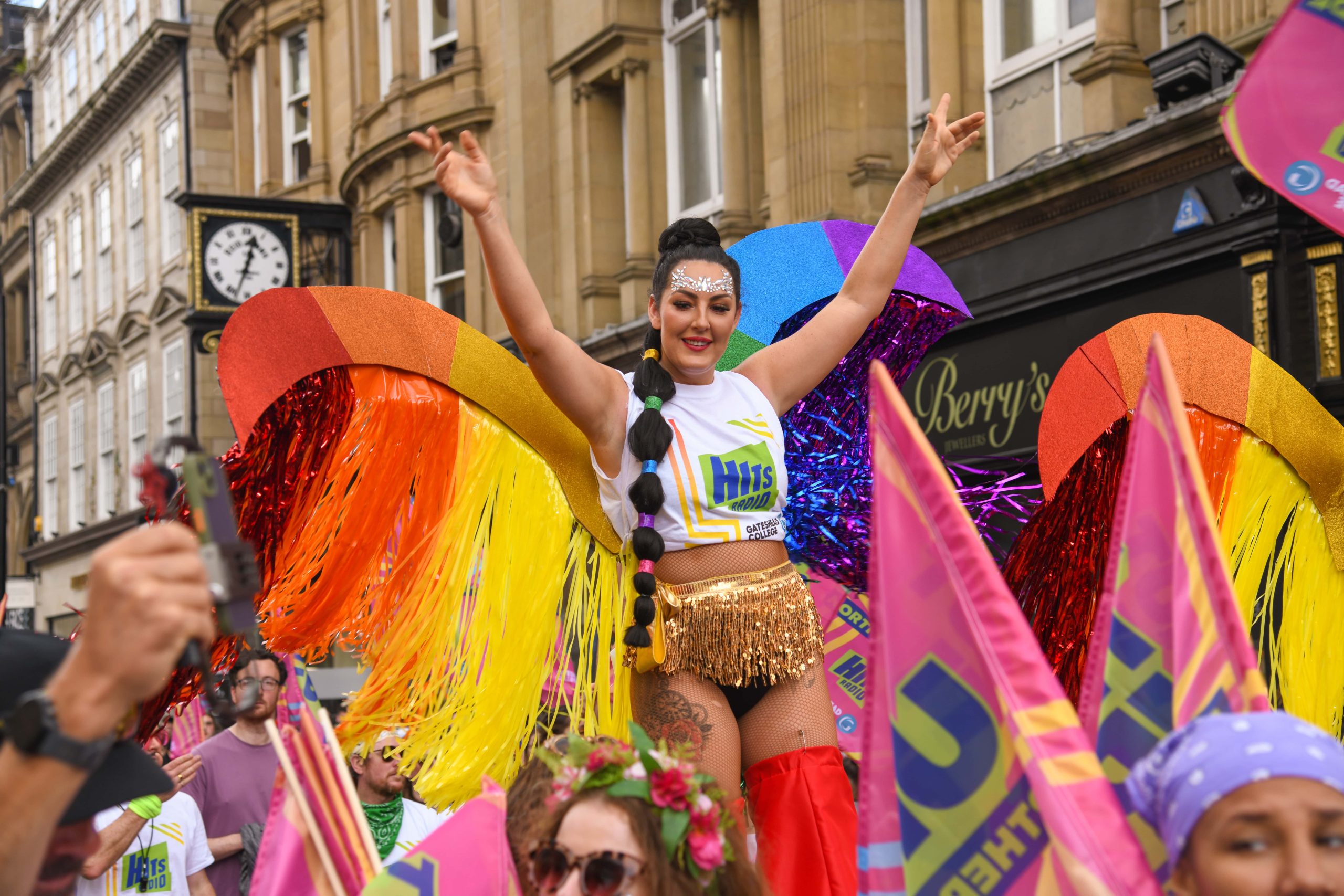 Person is colourful costume at the Pride March in Newcastle standing on stilts and cheering to camera.