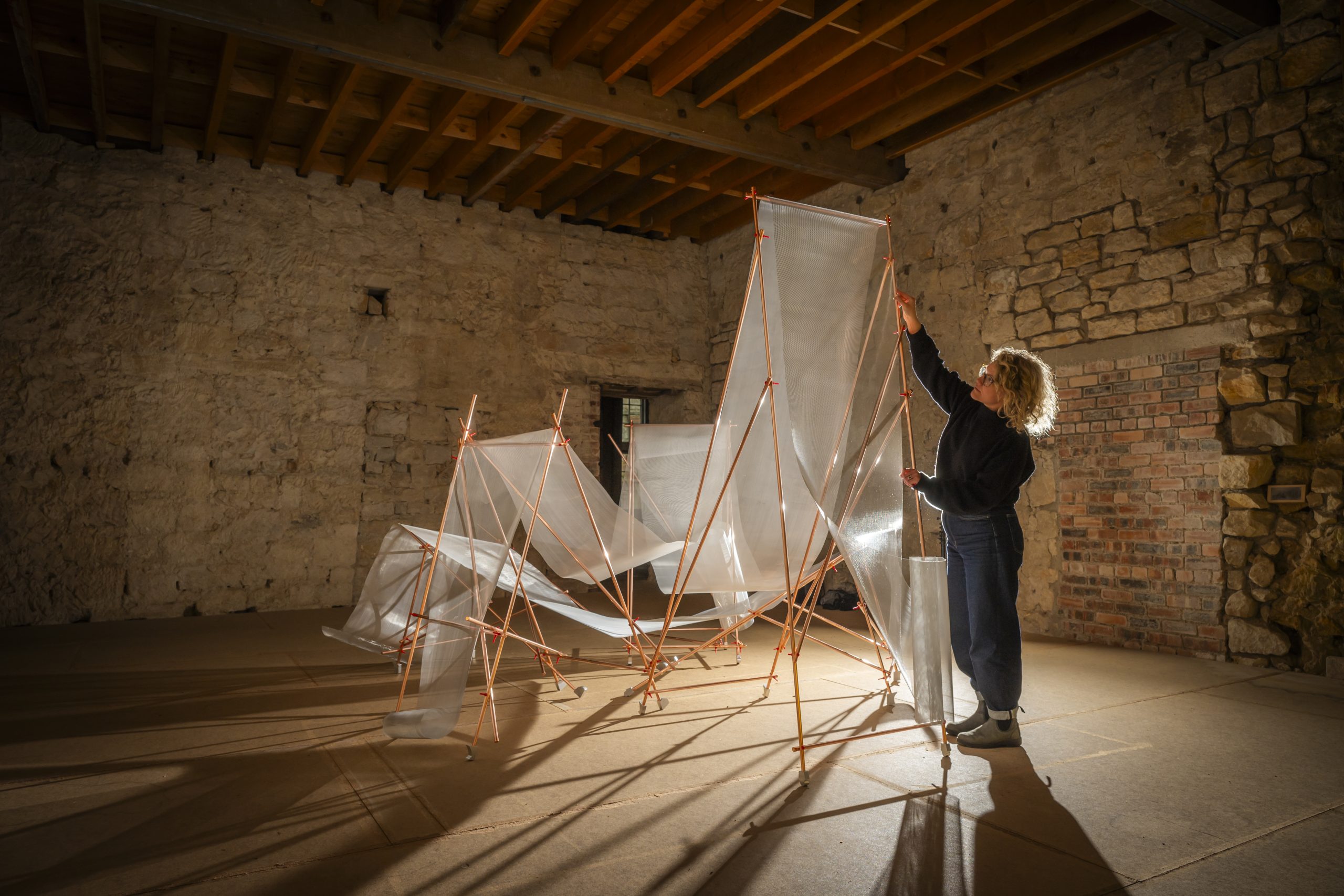 Art installation in the middle of a bare room with a person adjusting it.