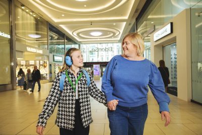 Mother and child walking through Eldon Square smiling at one another. The child is wearing ear defenders and green sunflower lanyard.