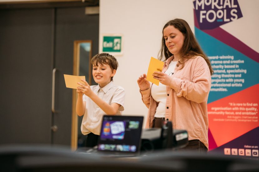 Adult and child reading flash cards in front of Mortal Fools banner.