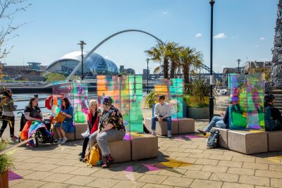 Groups of people sat in a colourful art installation by the River Tyne