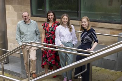 Four Muckle LLP team members stood on outdoor stairs smiling and posing naturally to camera.