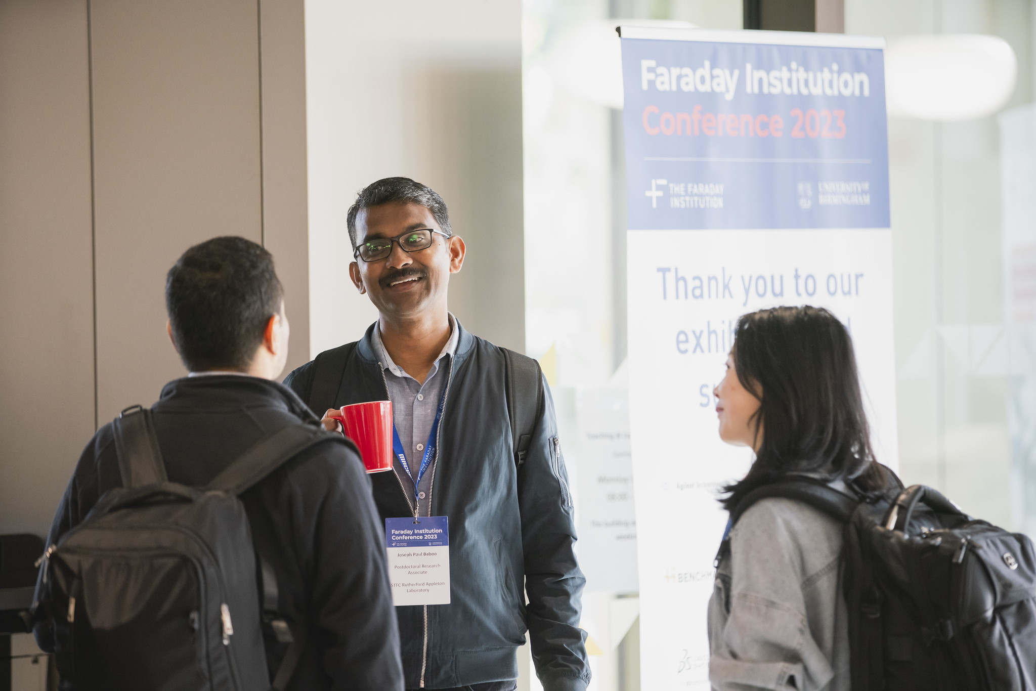 Three people networking in front of a Faraday Institution Conference banner.