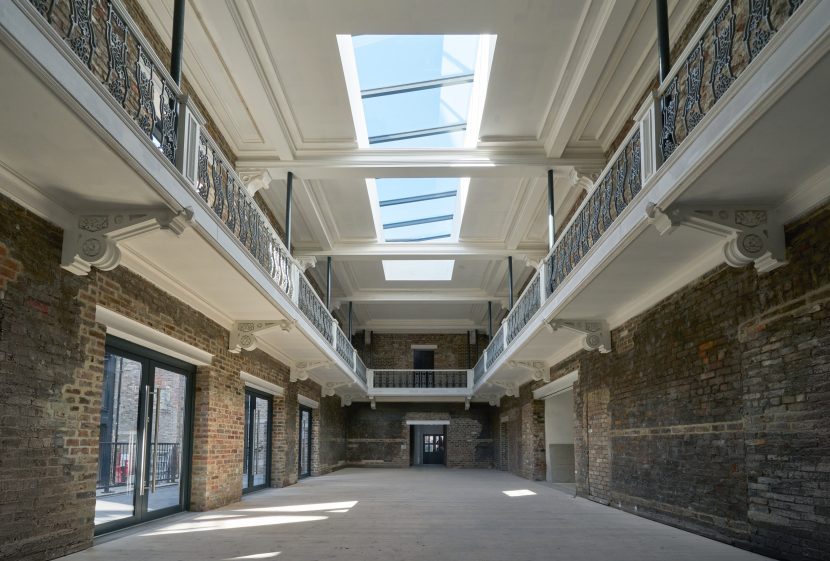 Interior of refurbished building with exposed brick walls and glass ceiling.