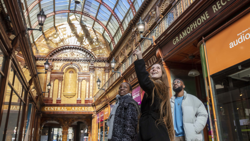 Three people is a glass ceilinged shopping centre one is pointing upwards and the others are looking up inspirationally.