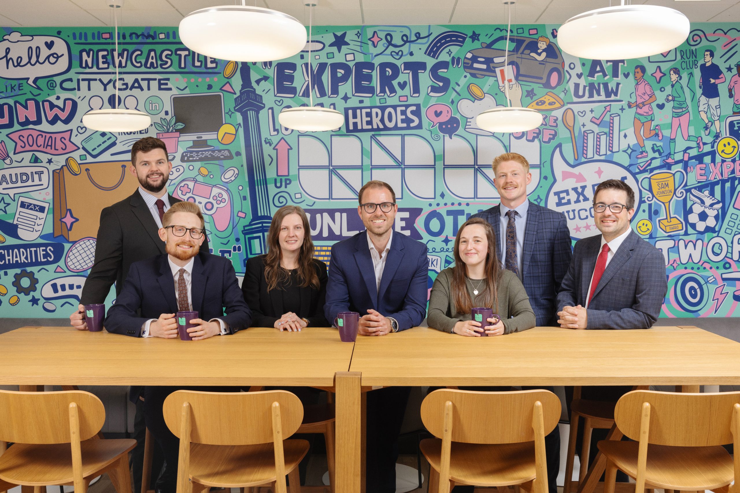 Peter Sym and colleagues sat at a wooden table in an office smiling to camera.