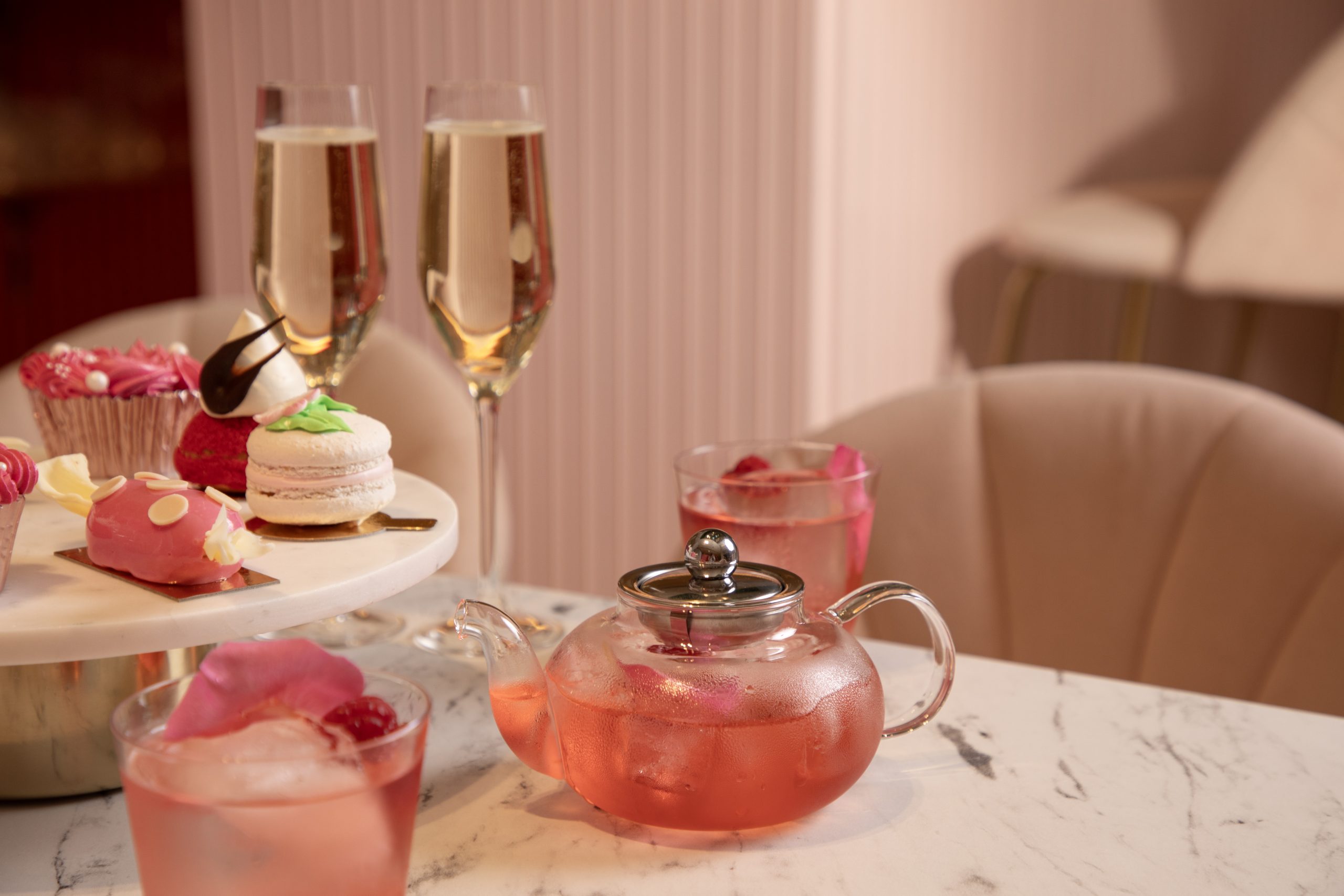 Table with two glasses of prosecco and cakes and cocktails.