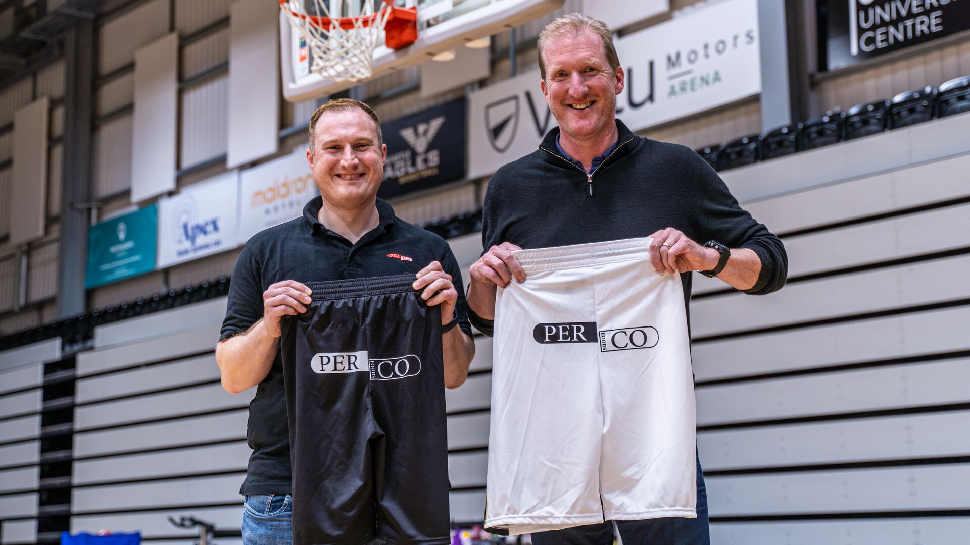 Daniel and Paul holding up basketball shorts with logo on the back in the Eagles stadium