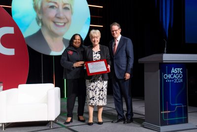 Linda accepting award on-stage in Chicago with two people stood on either side of her.