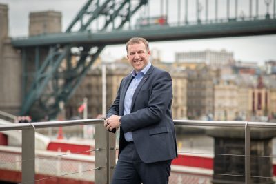 Chris Fraser leaning against the railings on the Aspire balcony overlooking the Swing Bridge and Tyne Bridge on Gateshead Quayside.