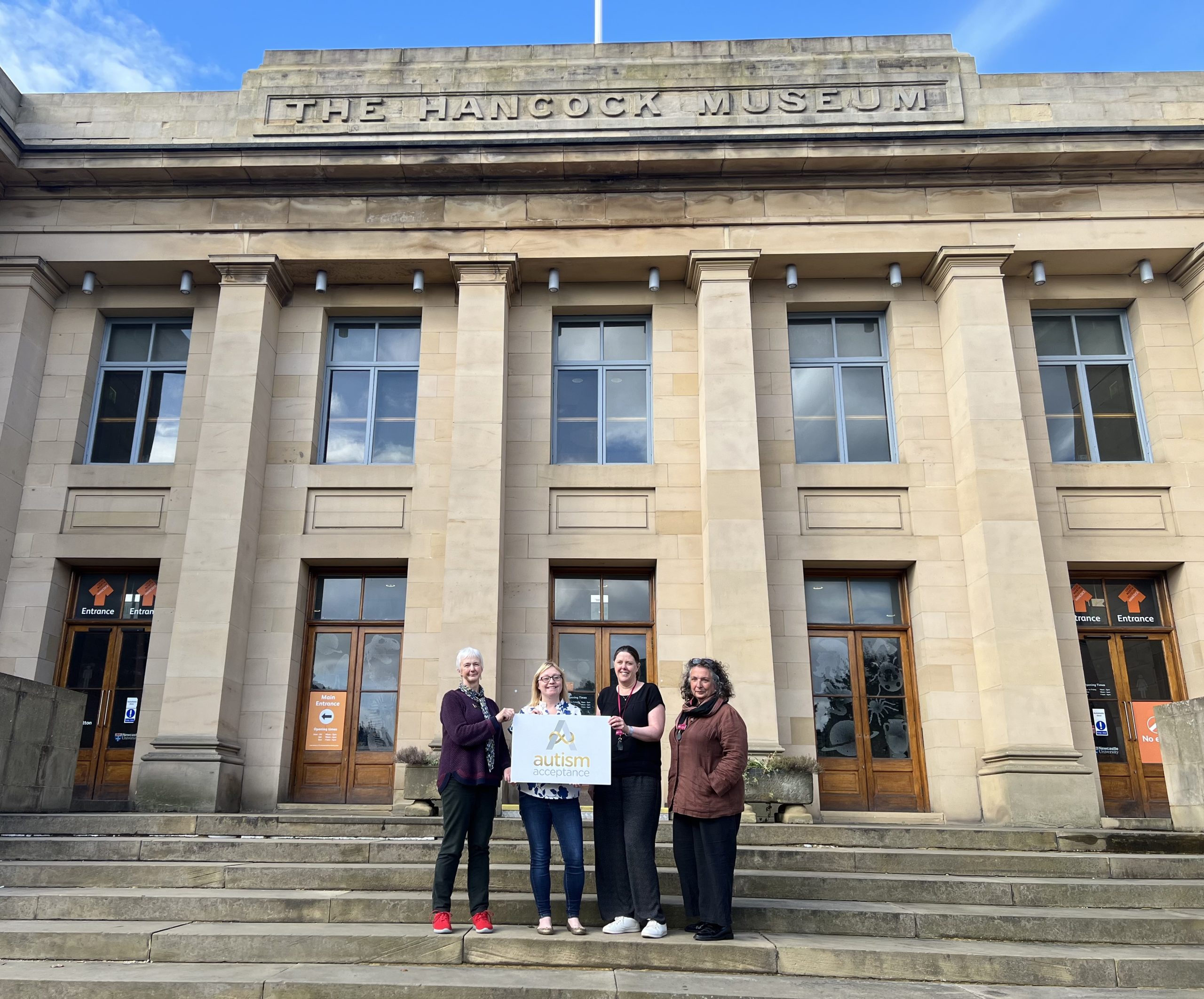 Four people stood outside of museum holding Autism Acceptance award