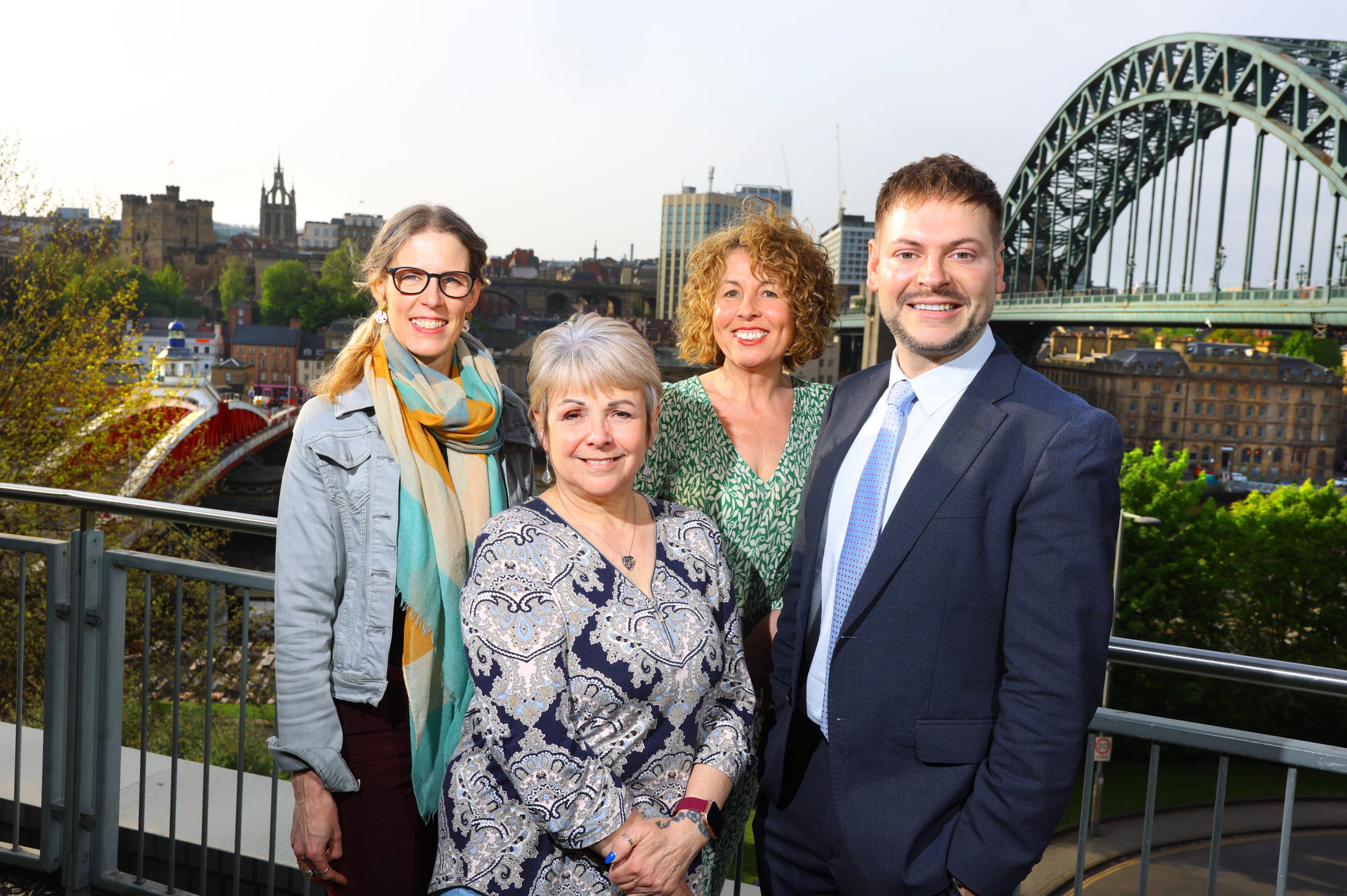 Four people smiling to camera on a balcony overlooking the terrace.