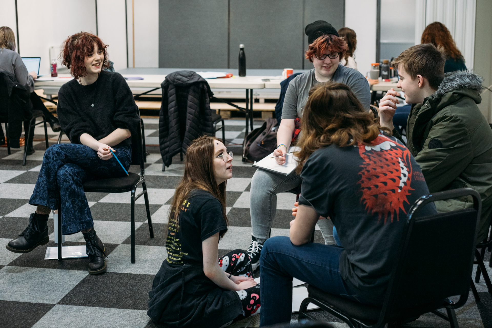 Group of young people sat on floor and on chairs chatting together.