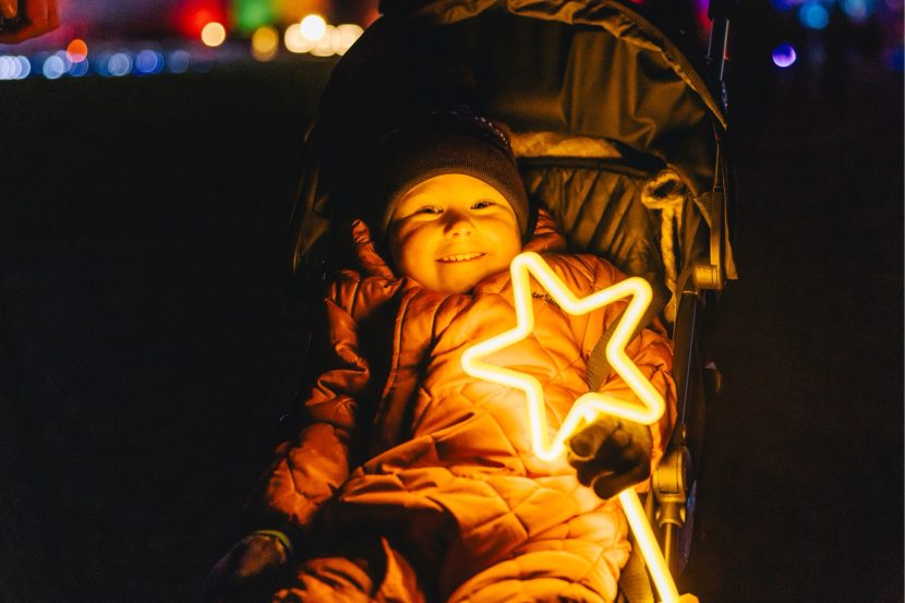 Child in a pram holding a light-up star smiling to the camera.