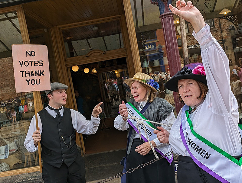 Three Beamish Museum staff members in 1900s costume dressed as suffragettes.