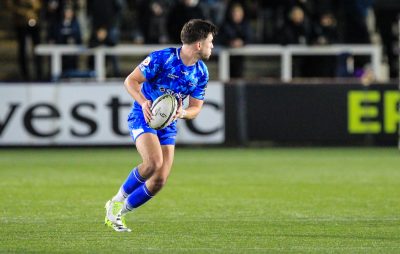 Rugby player on field dressed in blue uniform about to pass the ball in their hands.