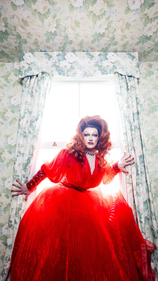 Kate Butch in red gown posing at a window.