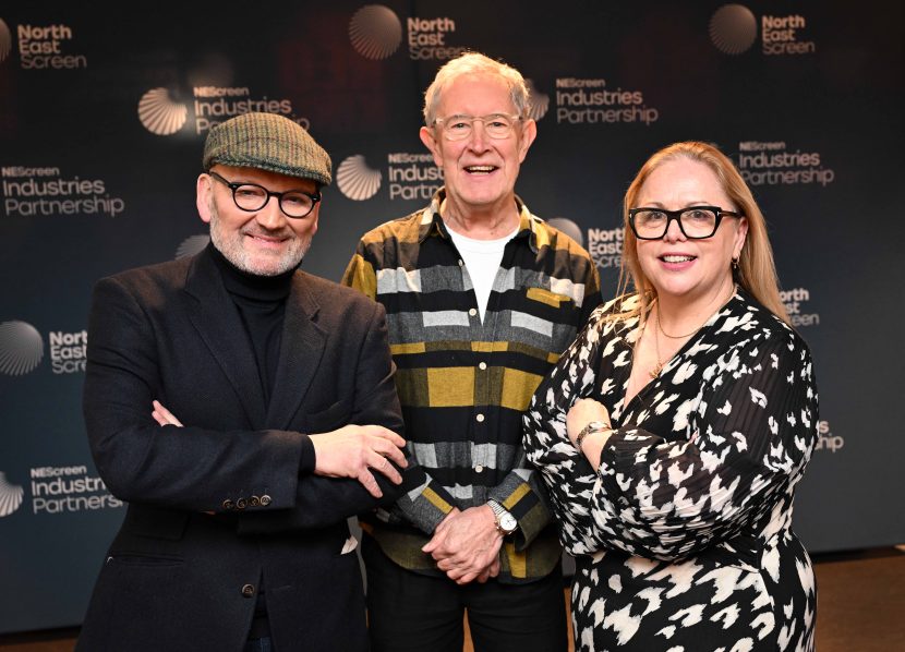 Three people stood closely together smiling to camera.