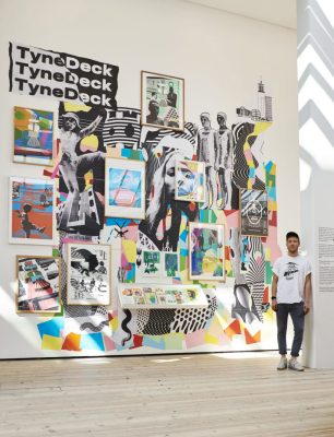 Jimmy Turrell stood next to a wall full of their collage-style artwork.