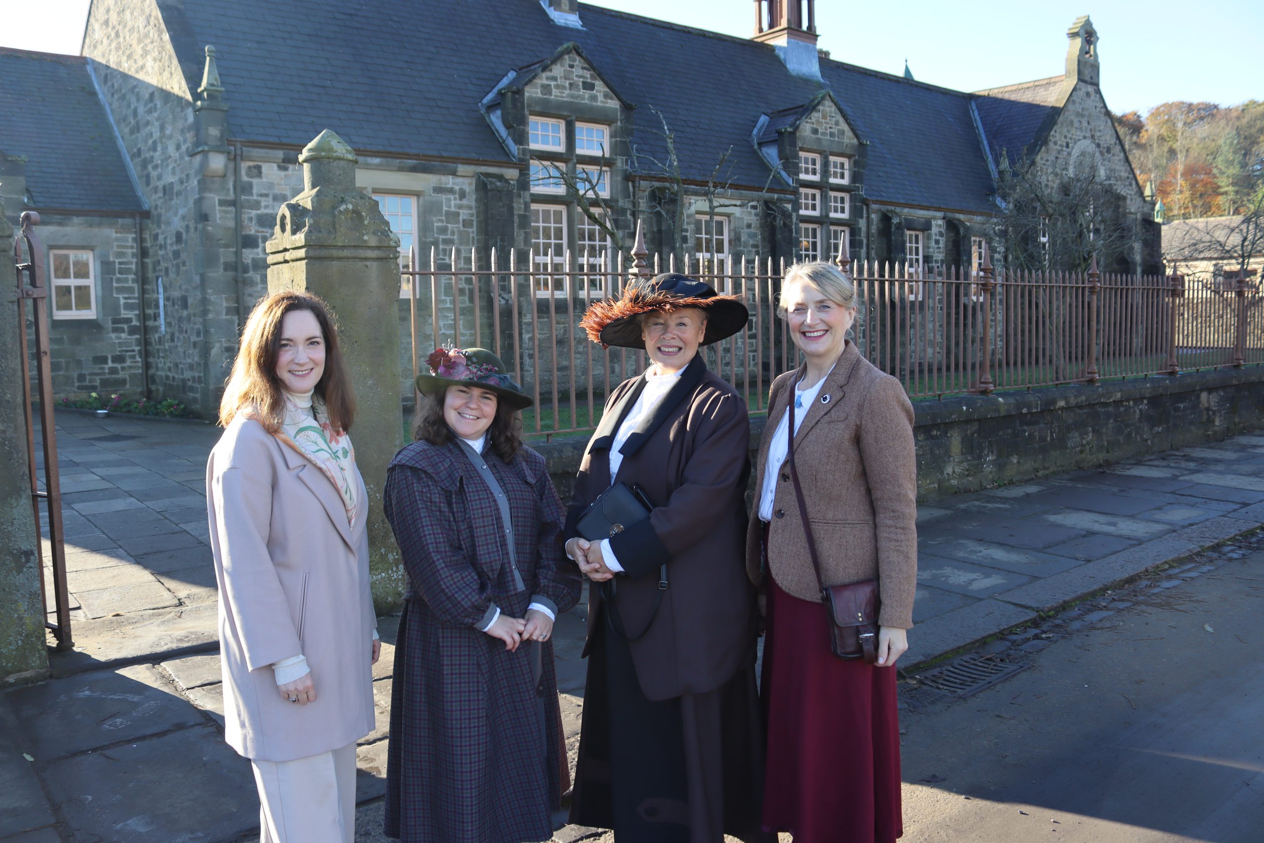 Four Beamish Museum staff members in vintage costumes posing outside of the Victorian school at the museum.