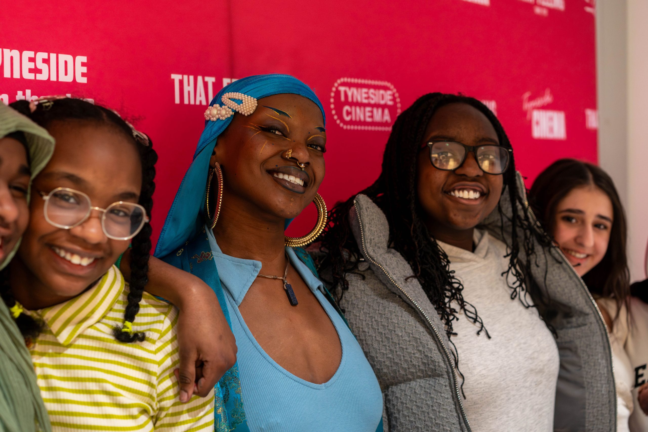 Five young people smiling to camera in front of a red Tyneside Cinema banner