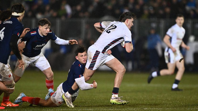 Rugby player in white kit running past opposition players with the ball in his hands.